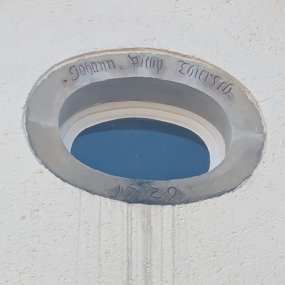 Das ovale Giebelfenster der alten Bäckerei von Kirchscheidungen. Es war wohl ursprünglich über der Haustür des Backhauses platziert. 1872 wurde das Backhaus abgerissen und 90° dazu ein Wohnhaus errichtet.   J. P. Thiersch war der erste Thiersch in Kirchscheidungen (1689–1757). Er baute 1629 das Backhaus an der heute noch so bezeichneten Backlücke. Johann Samuel Benjamin Thiersch (1753–1832), die Hauptperson in der Novelle, war sein Enkel. Er heiratete 1780 die Pfarrerstochter Henriette Lange (1762–1813). Sie hatten neun Kinder, darunter Bernhard und Friedrich Wilhelm Thiersch.